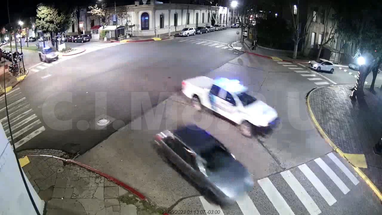 imagen borrosa de cámara de seguridad vista desde arriba de la avenida que muestra un auto seguido de un patrullero