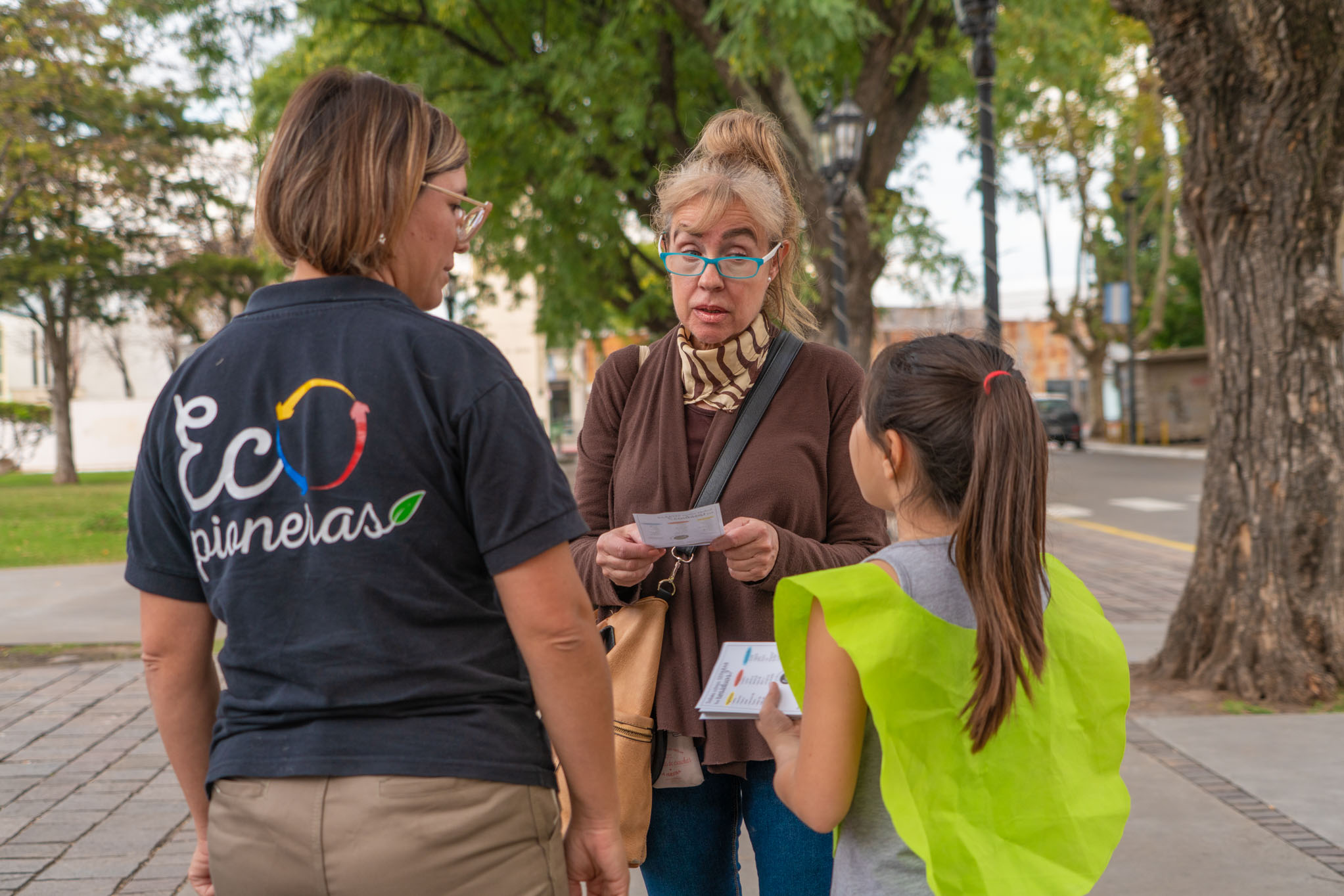 Nena de entre 6 a 8 años de edad militando el reciclaje a una señora de la tercera edad acompañada de un adulto femenino que pareciera ser su madre u otro elemento de la municipalidad. 