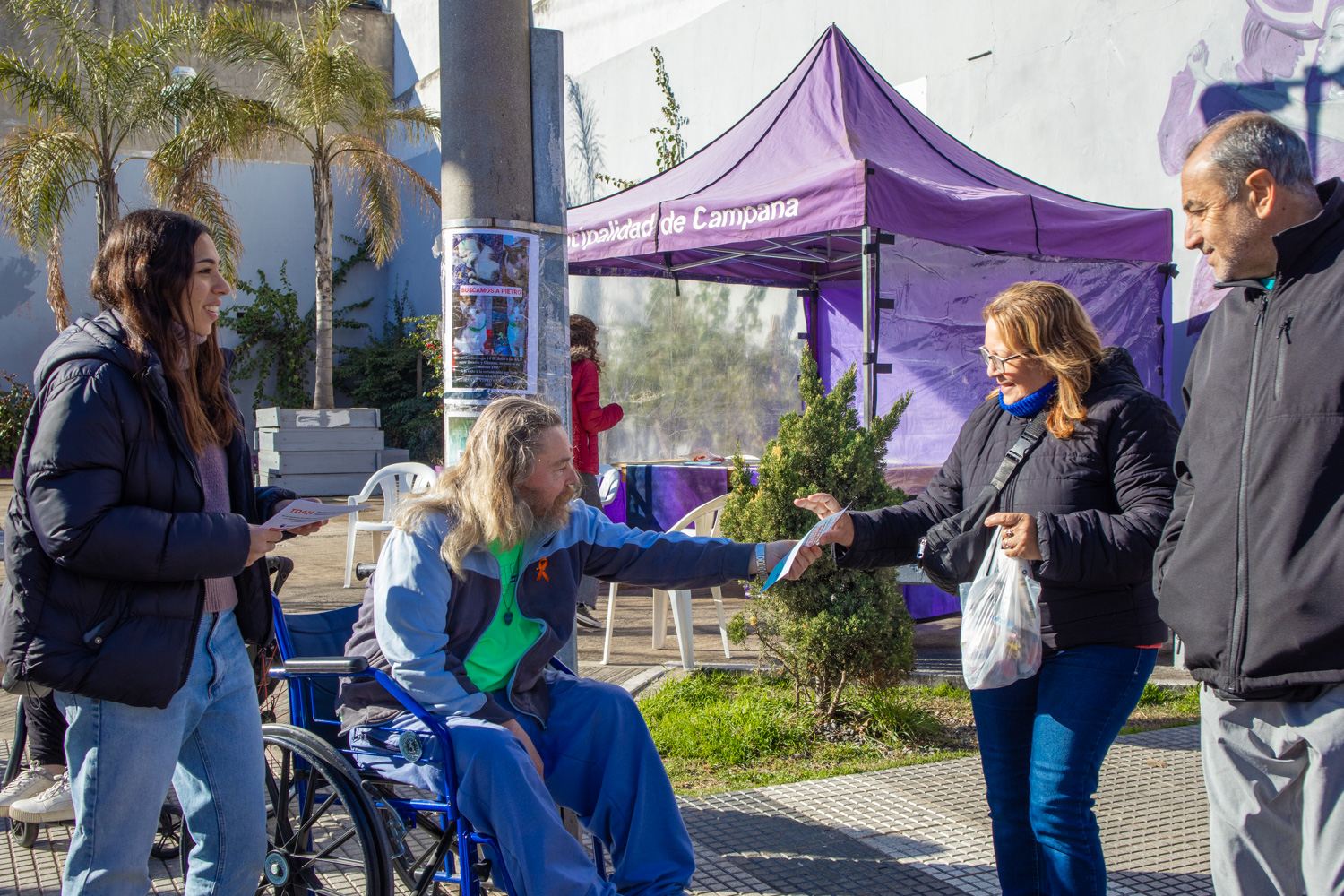 Vecino residente del Hogar Municipal de Discapacidad entregando folletería a una pareja que pasan caminando